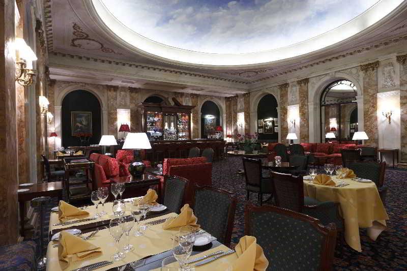 Hotel Le Plaza Brusel Exteriér fotografie The photo depicts an elegant restaurant interior. The space features ornate decor, with a large, beautifully painted ceiling that gives an open and airy feel. The walls are adorned with rich textures and possibly artwork. 

Tables are set with yellow