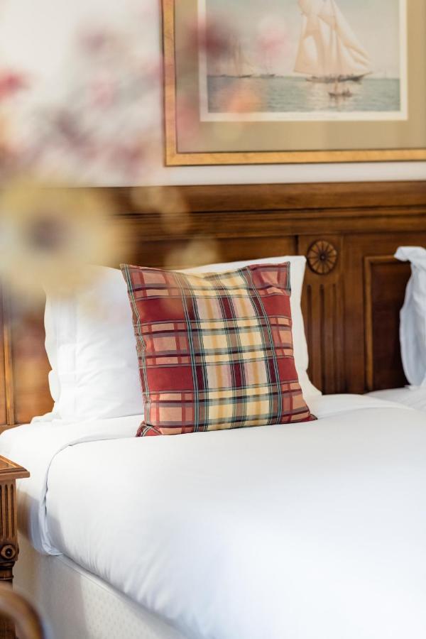 Hotel Le Plaza Brusel Exteriér fotografie The photo shows a decorative plaid pillow placed on a bed. The pillow features a mix of red, yellow, and dark plaid patterns. The bedding is white, and there is a wooden headboard in the background, which has a decorative design. The overall ambiance
