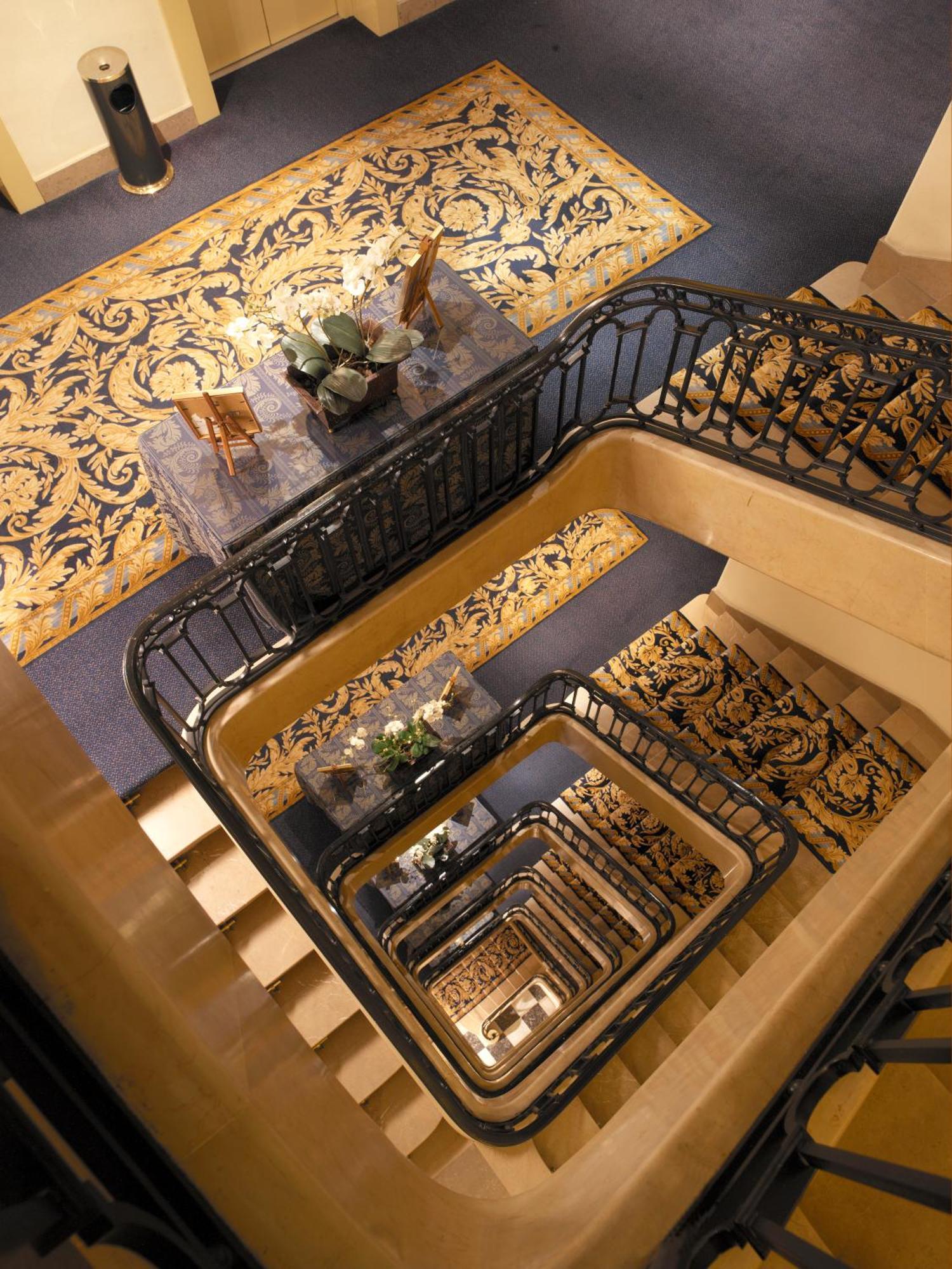 Hotel Le Plaza Brusel Exteriér fotografie The photo shows a staircase viewed from above, featuring a series of descending steps that curve around a central area. The walls and railings are elegantly designed, with a decorative black metal railing. At the top of the stairs, there is a small t